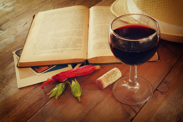 Red wine glass and old book on wooden table at sunset burst