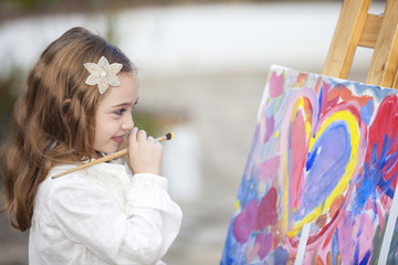 Niña de seis años sonriente pintando un cuadro en exteriores