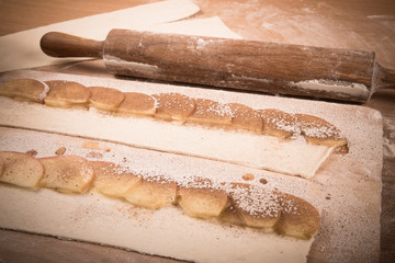 Apple slices on stripes of dough and rolling pin on a light wood
