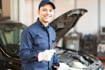 Portrait of a smiling mechanic holding a wrench - obrazy, fototapety, plakaty