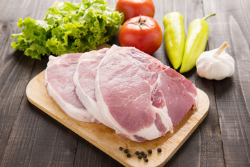 Raw pork on cutting board and vegetables on wooden background