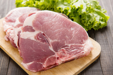 Raw pork on cutting board and vegetables on wooden background
