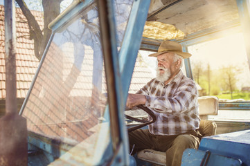 Fototapeta na wymiar Senior man at the farm driving an old tractor