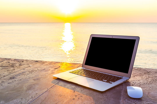 laptop on table at sea sunset in summer time