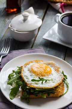 crispy toast with a fried egg and fresh arugula, a cup of coffee