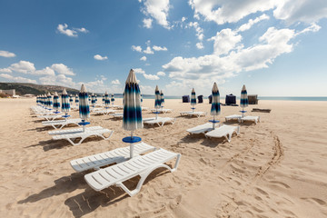 chairs and closed umbrellas on beach. 