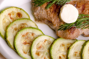 Pork steak, grilled, with melting butter and zucchini, top view