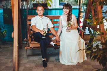 Obraz premium happy bride and groom drink mojito, swinging on a swing