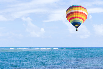 Hot air balloon over ocean and clouds blue sky