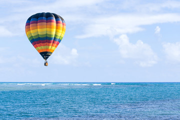 Hot air balloon over ocean and clouds blue sky