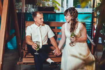 Fototapeta premium happy bride and groom drink mojito, swinging on a swing