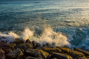 Sea waves hit the rock at sunset