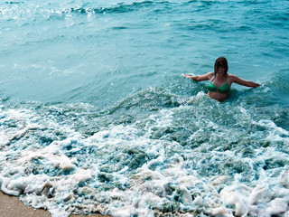 Pretty laughing girl in foaming waves of blue sea