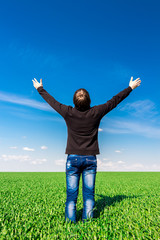 Man dressed in black shirt and blue jeans among blue sky and green field
