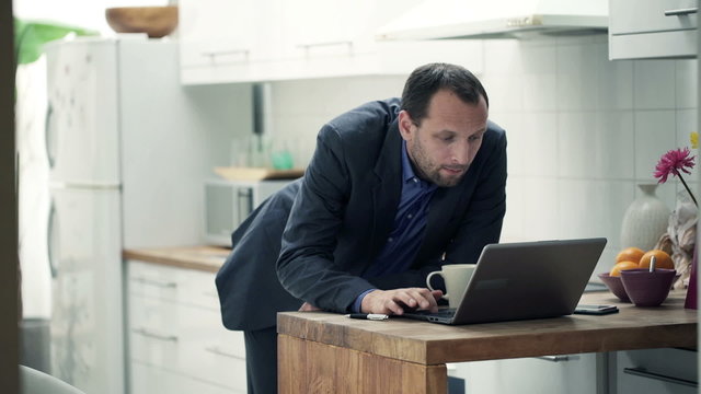 Businessman with laptop drinking coffee in kitchen 
