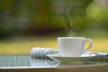 Cup of coffee with smoke and newspaper in garden