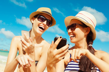 Happy beautiful women using mobile smart phone at the beach