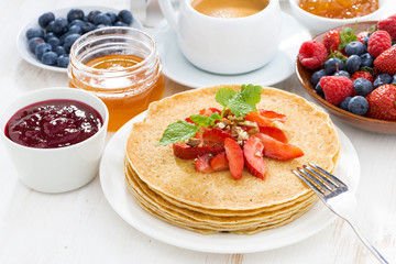 crepes with strawberries and honey on white wooden background