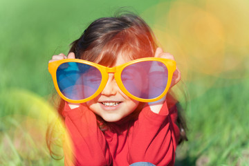 Happy smiling little girl wearing big sunglasses in the field