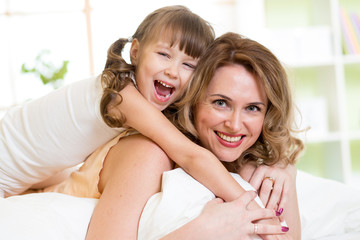 Woman and kid girl in bed playing and smiling