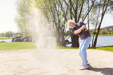 Old golf player pitching from bunker.