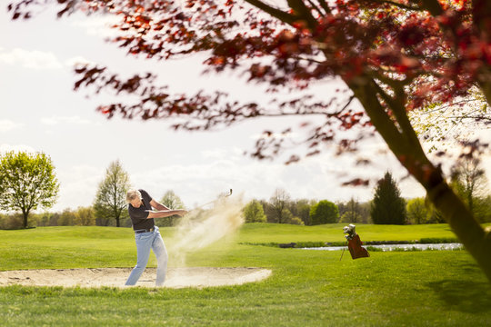 Male golfer playing from sand bunker hazard. - Powered by Adobe
