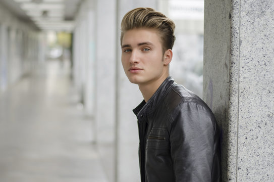 Young man with leather jacket standing outside against pillar