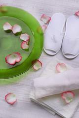 Spa bowl with water, rose petals, towel and slippers on light background. Concept of pedicure or natural spa treatment