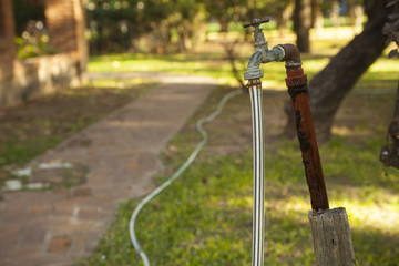 Old rusty water tap with hose in garden