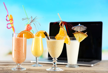 Laptop and glasses of summer cocktails on wooden table, on bright blurred background