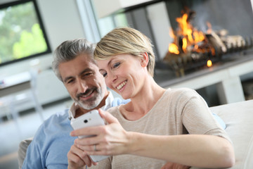 Mature couple at home having fun using smartphone