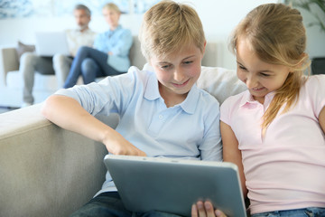Fototapeta na wymiar Kids using digital tablet at home, parents in background