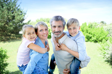 Parents giving piggyback ride to kids in garden