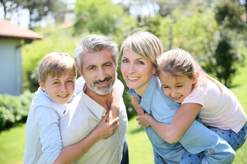 Fototapeta premium Parents giving piggyback ride to kids in garden