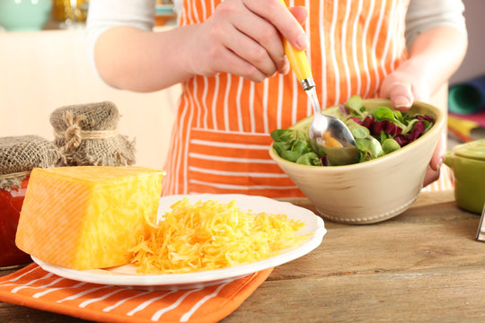 Woman cooking salad with grating cheese, close-up