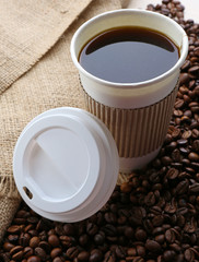 Paper cup of coffee with beans on sackcloth close up