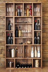 Shelving with wine bottles with glasses on wooden wall background