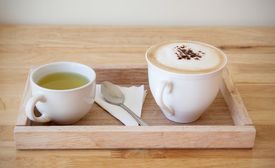 Cappuccino and hot green tea on a wooden tray.