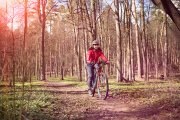 Fototapeta premium Young woman riding a bicycle through forest