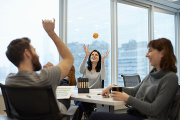 Three business people, two women and a man, reaching up to catch a ball.