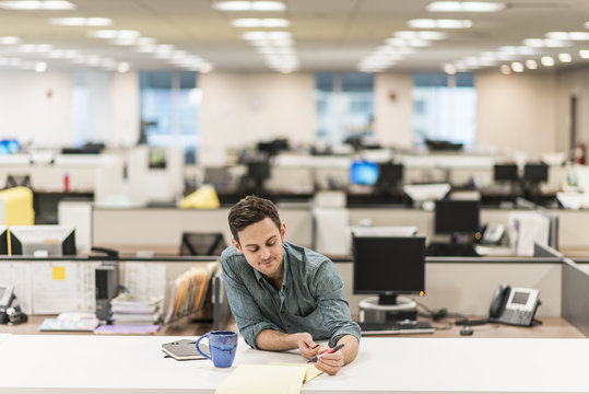 A young man seated at a desk in an office holding a pen.