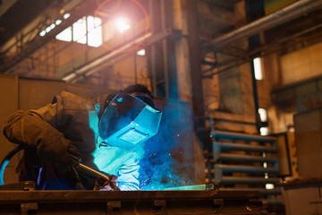 Young man with protective mask welding in a factory - obrazy, fototapety, plakaty