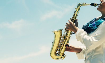 Saxophonist playing on saxophone on blue sky background