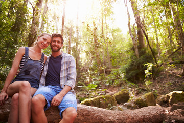 Couple Sitting On Tree Trunk In Forest Together