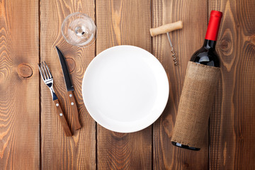 Table setting with empty plate, wine glass and red wine bottle