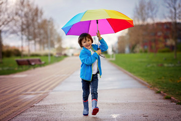 Cute little boy, walking in a park on a rainy day, playing and j