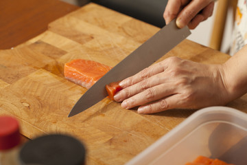 an Asian woman chef preparing salmon piece with sharp knife