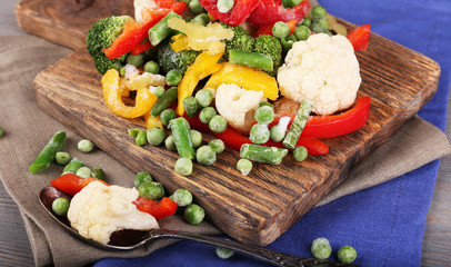 Frozen vegetables on cutting board, on napkin, on wooden table background