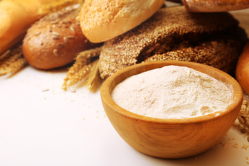 Fresh bread with wheat, sesame, sunflower seeds and wooden bowl of flour, closeup