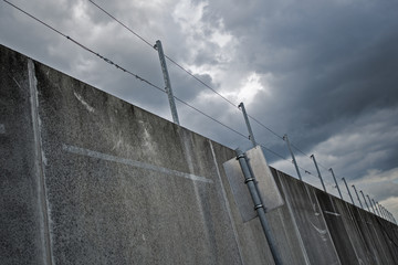concrete wall weathered with barbedwire on top under cloudy sky